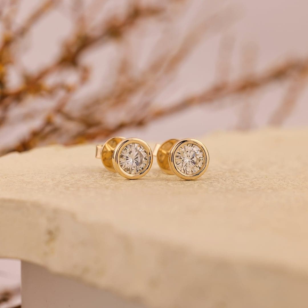 Pair of gold stud earrings with clustered round diamonds on a stone surface