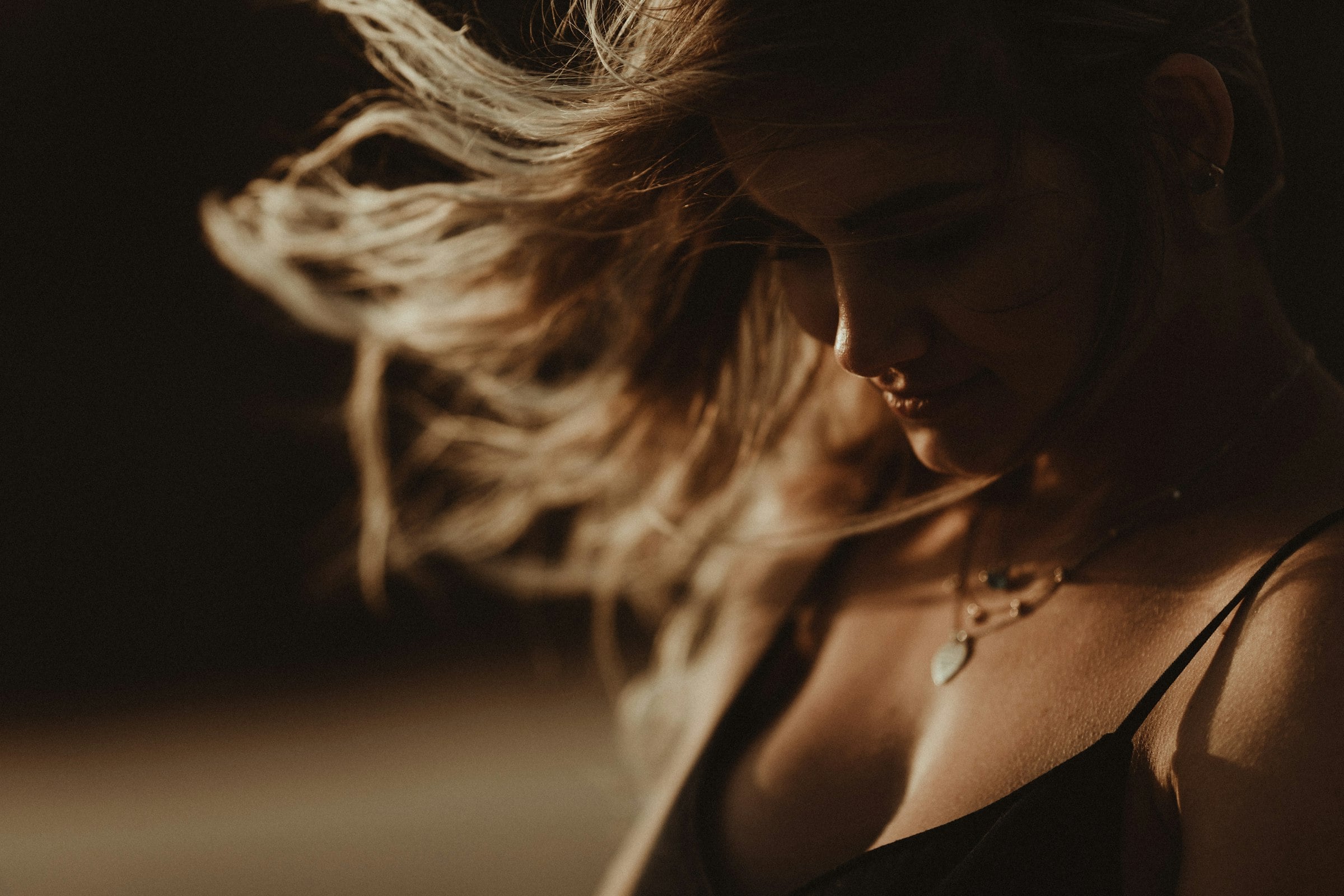 Woman in a black camisole wearing a delicate pendant necklace, lit by warm evening light