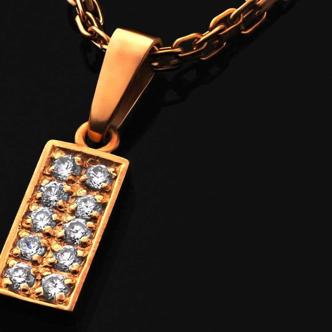 Close-up detail — gold chain necklace with a rectangular pavé diamond pendant against a black background