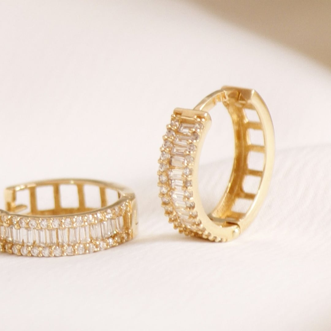 Close-up detail — gold huggie hoop earrings set with diamonds on ivory satin