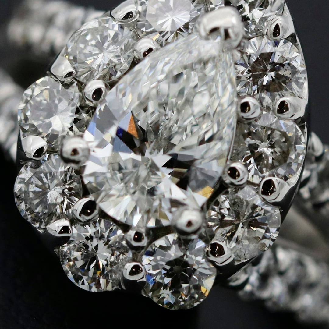 Close-up detail — pear-shaped diamond halo ring with a pavé band on dark fabric