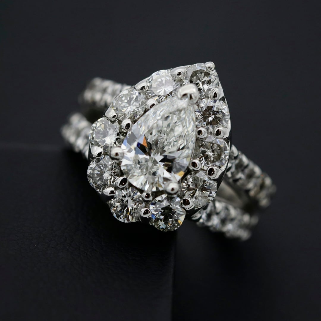 Pear-shaped diamond halo ring with a pavé band on dark fabric